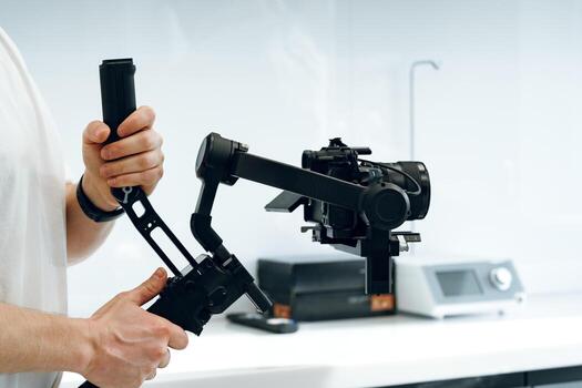 A person operates a handheld gimbal stabilizer with a camera in a modern studio setting during a daytime shoot photo