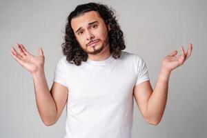 A man with curly hair expressing uncertainty while standing against a neutral background photo