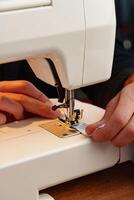 Hands sewing fabric using a sewing machine on a wooden table in a well-lit workspace photo