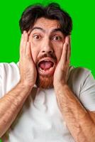 A man with a surprised expression holds his face while against a vibrant green background photo