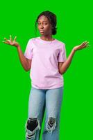 A young woman in casual attire smiles playfully with hands raised in a questioning gesture against a bright green background photo