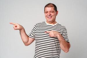 Man dressed in a white polo shirt and jeans happily pointing to the side against a plain background photo
