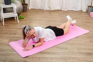 Woman doing floor exercises on a pink mat in a bright room photo