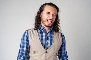 Man making a silly face with tongue out in casual attire against a neutral background photo