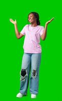 A young woman in casual attire smiles playfully with hands raised in a questioning gesture against a bright green background photo