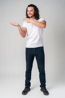 Young man in a white t-shirt and jeans pointing confidently while smiling in a studio setting photo
