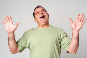 A middle-aged man with a neutral expression raises his hands in a questioning gesture against a plain backdrop photo