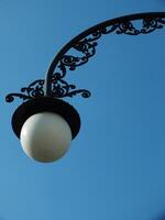 A street light with a white bulb is lit up against a blue sky. The light is on a metal pole with a decorative design. The scene is peaceful and serene photo