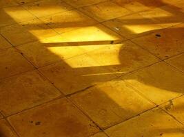 A yellow floor with a shadow on it. The floor is made of tiles and the shadow is on the floor. Vintage ambience on old building interior photo