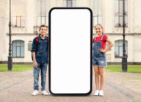 Two young siblings pose beside a large, empty mobile phone frame in front of an elegant building. They look cheerful and excited to showcase a unique display in this beautiful location. photo