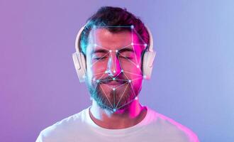 A young man with a beard listens to music while wearing headphones, enjoying a moment of relaxation. Colorful lights enhance the ambiance around him, showcasing facial recognition patterns. photo