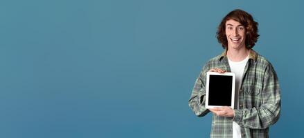 Curly millennial guy holding tablet computer with blank screen on color background, mockup for your design photo