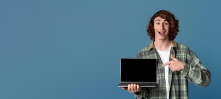 Excited millennial guy pointing at laptop computer with empty screen on turquoise background, space for your ad photo