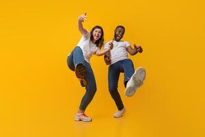 Yo. Positive interracial couple fooling together, having fun and laughing at camera over yellow studio background, low angle view photo