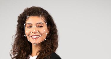 A young woman with curly hair smiles while facial recognition technology is applied, highlighting key facial features through a network of points. She exudes confidence in a simple outfit. photo