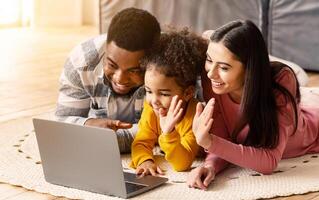 Online communication during home isolation. Mom and daughter waving their hands in laptop, dad smiling photo