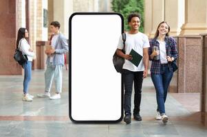 A diverse group of students strolls through a university corridor, pass by huge phone with blank screen, engaging with each other. photo
