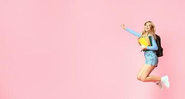 Yes, I Have Done It. Happy student girl wearing backpack jumping at studio, holding notebooks. Free space, full length photo