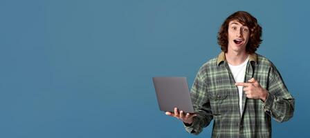 Lottery winner. Funky teenager pointing at laptop and shouting OMG on turquoise background photo