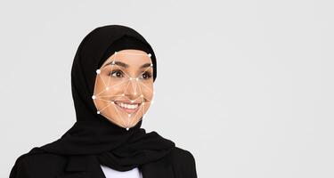 A woman wearing a black hijab smiles while participating in a technology event, where facial recognition technology is demonstrated. The setting highlights advancements in digital innovation. photo