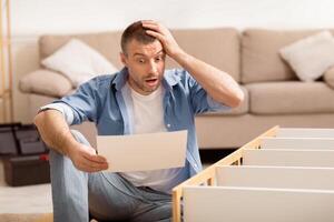Shocked Man Assembling Furniture Scratching Head Reading Difficult Manual Inctruction Furnishing House Sitting Indoor. Selective Focus photo