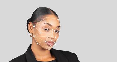 A young black woman in formal attire stands confidently while a facial recognition overlay is displayed on her face. The background is minimally styled, highlighting her expression and technology. photo