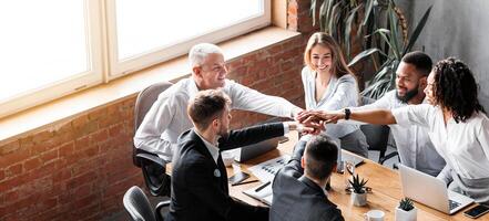Teamwork. United Business Team Of Colleagues Holding Hands Sitting Together At Table In Modern Office. High-Angle Shot, Empty Space photo