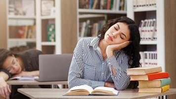 Exam Time. Tired mexican girl reading a book and asian guy sleeping in the university library in the background photo
