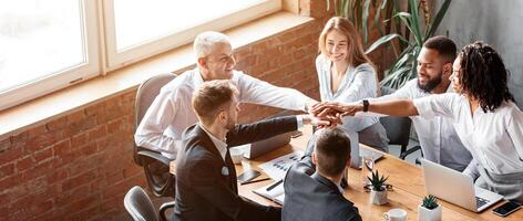 Teamwork And Partnership. Multiracial Business People Holding Hands Together Sitting At One Desk In Modern Office. High Angle, Free Space photo
