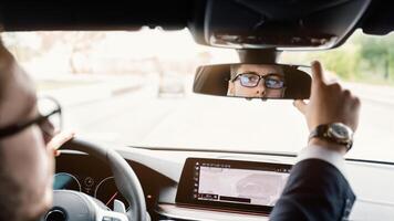 Close up back view portrait of man in specs adjusting rearview mirror while sitting in his car, selective focus photo