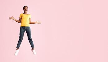 Excited African Millennial Lady Jumping And Shouting In Joy Over Pink Background. Studio Shot, Full Length, Copy Space photo
