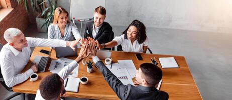 Corporate Spirit. Happy Business Team Giving High-Five Celebrating Success At Work Sitting At Desk In Modern Office. High Angle photo