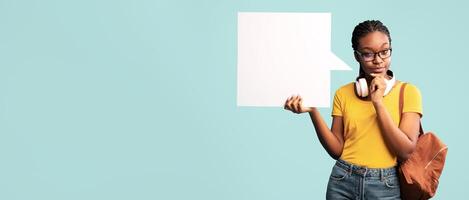 Thoughtful Black Student Lady Showing Empty Speech Bubble Thinking About Something Posing Over Blue Studio Background. Mockup photo