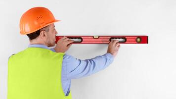 Housebuilder Workman Using Building Level Working Standing Back To Camera On White Studio Background, Wearing Orange Uniform. Builder Using Measurement Tools At Construction Site. Rear View, Panorama photo
