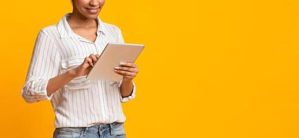 Useful Devices. Unrecognizable African American Woman Using Digital Tablet, Standing Over Yellow Background, Cropped Image, Panorama With Free Space photo