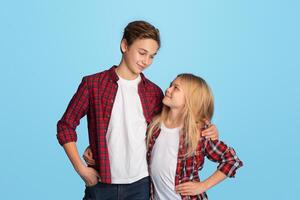 Siblings Love. Portrait of happy preteen brother and sister embracing and looking at each other, posing over blue background in studio, copy space photo