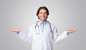 Friendly male doctor demonstrating invisible objects on his open palms, posing over light background, panorama with copy space photo