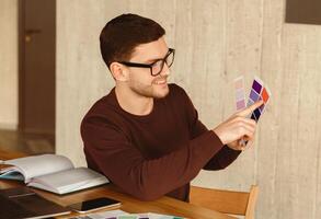 Designer Guy Choosing Color Samples For His Project Sitting At Workplace In Modern Office. Selective Focus photo