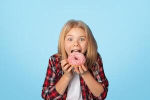 Unhealthy Sweets. Portrait Of Brother And Sister Eating Sugary Donuts And Looking At Camera, Posing Over Blue Background With Free Space photo