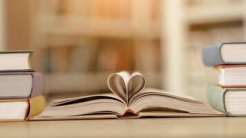 Love Story. Open book with pages in heart shape lying on the reading desk in library, piles of old manuals on the sides photo