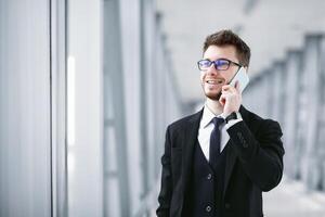 Always In Touch Concept. Handsome entrepreneur talking on phone, wearing eyeglasses, blurred background photo
