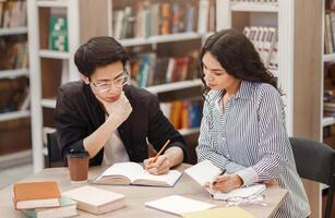 Studying Together. Concentrated multicultural couple doing homework, helping each other sitting at table in library photo