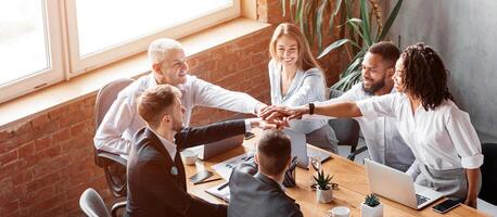 Teamwork And Unity. Business Colleagues Holding Hands During Corporate Teambuilding Meeting Sitting Together At Desk In Modern Office. photo