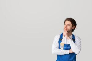 House Renovation Ideas. Portrait Of Pensive Laborer In Work Uniform Touching Chin And Looking Away Deep In His Thoughts, Panorama With Copy Space photo