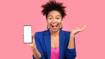 Excited Afro Girl Showing Phone With Empty Screen Smiling At Camera Standing Over Pink Studio Background. Mock up photo