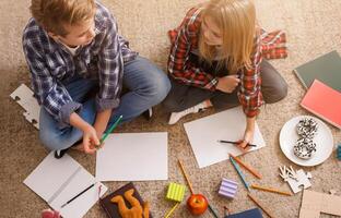Homework Concept. Brother And Sister Sitting On Floor And Sketching At Home. Top View photo