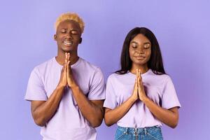 Peaceful black couple putting hands together in namaste or prayer gesture on lilac background photo