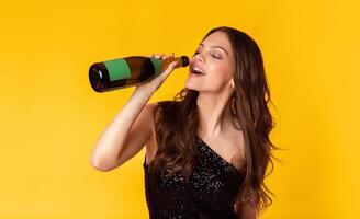 Party Hard Concept. Portrait of young woman in sequin dress drinking from the bottle of champagne, standing over colorful background in studio, free space photo