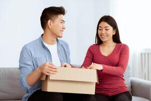 Changing Apartments. Filipino family sitting on sofa and unpacking cardboard boxes, free space photo