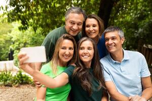 A group of five friends gathers in a park, smiling and posing together for a fun selfie amidst lush greenery on a sunny day. Their joy captures the essence of friendship. photo